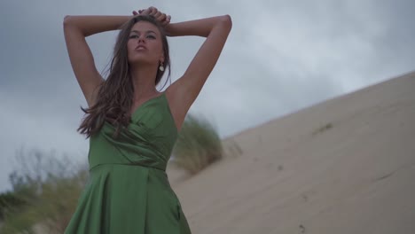 professional dark haired women posing confidant thinkful and seductive on a sand dune beach with cloudy sky - photo shooting - cinematic slowmotion