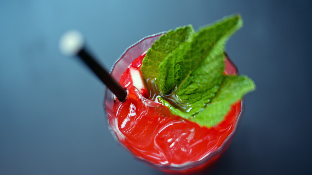 A red drink with ice and mint in a transparent glass, on a blue background