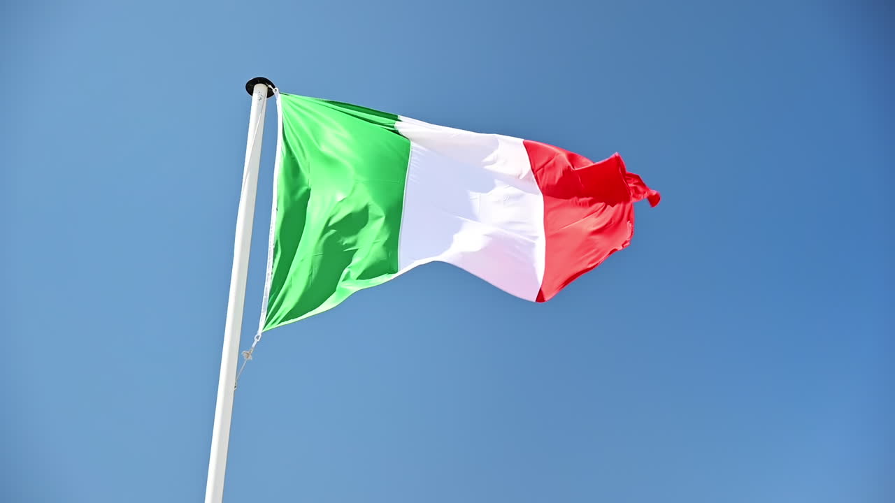 La bandiera italiana sventola al vento sul pennone. Cielo blu sullo sfondo. Rallentatore