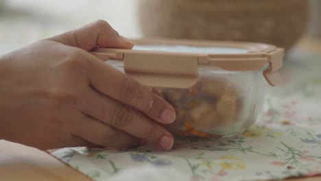 woman's hand opening a food container on a table with a floral tablecloth