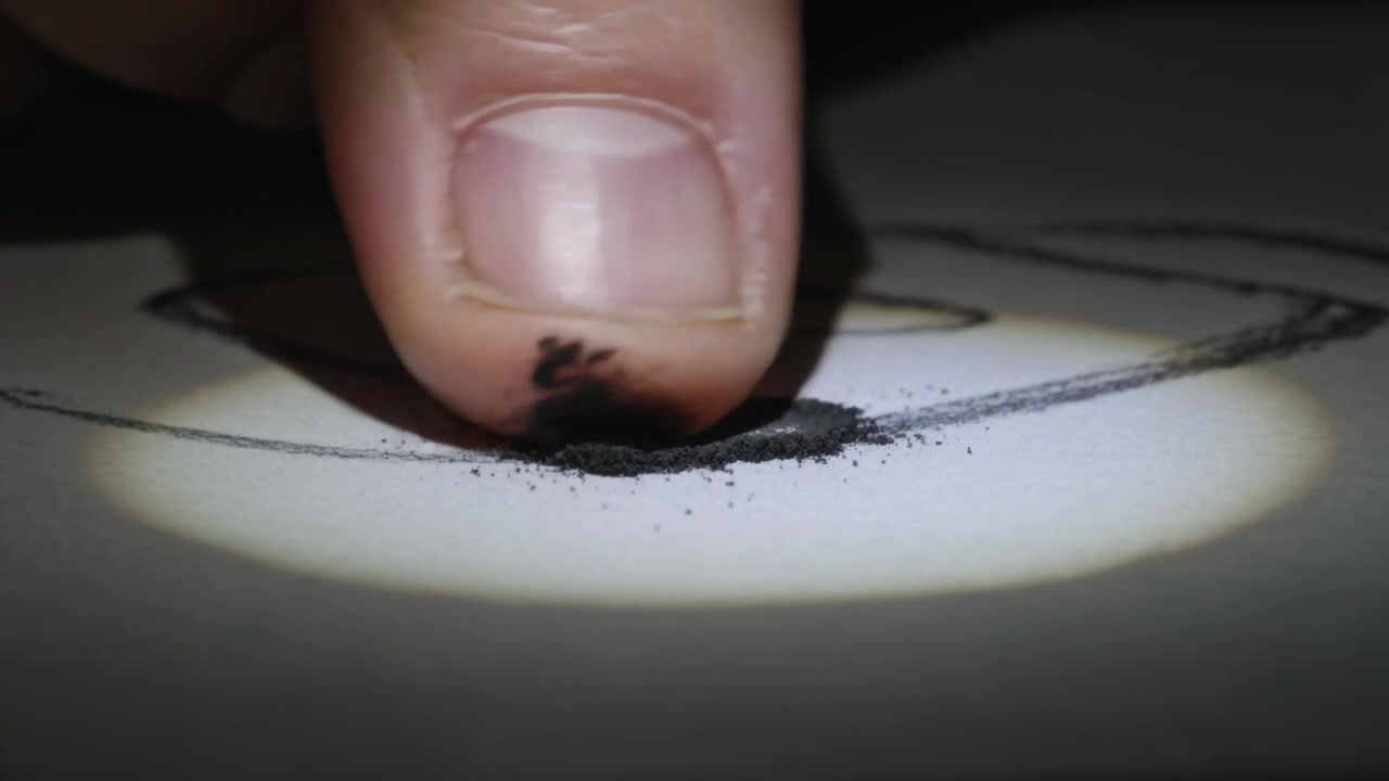 Hovering fingertip lowering onto paper on desk rubbing lead inside pencil oval for shading in beam