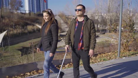un hombre ciego caminando por el parque charlando con su esposa.