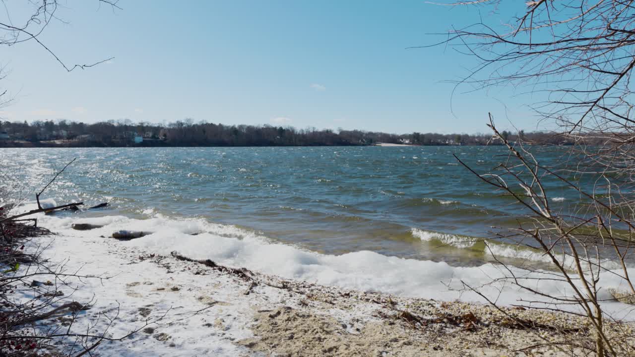 A peaceful winter scene at Lake Ronkonkoma, Long Island. Clear blue skies reflect over shimmering icy waters, creating a tranquil moment of natural beauty. Captures the serene charm of the season.