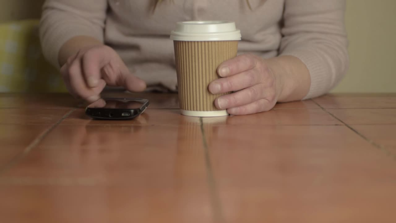 manos sosteniendo un café para llevar con una toma amplia del teléfono