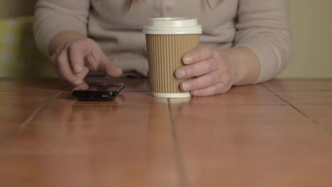 hands holding a takeaway coffee to-go with phone wide shot