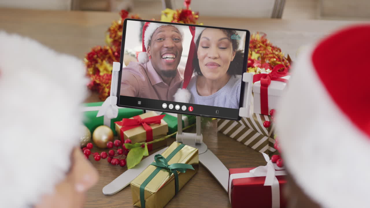 animación de una pareja diversa con sombreros de santa en una llamada de video de tableta con una pareja en navidad