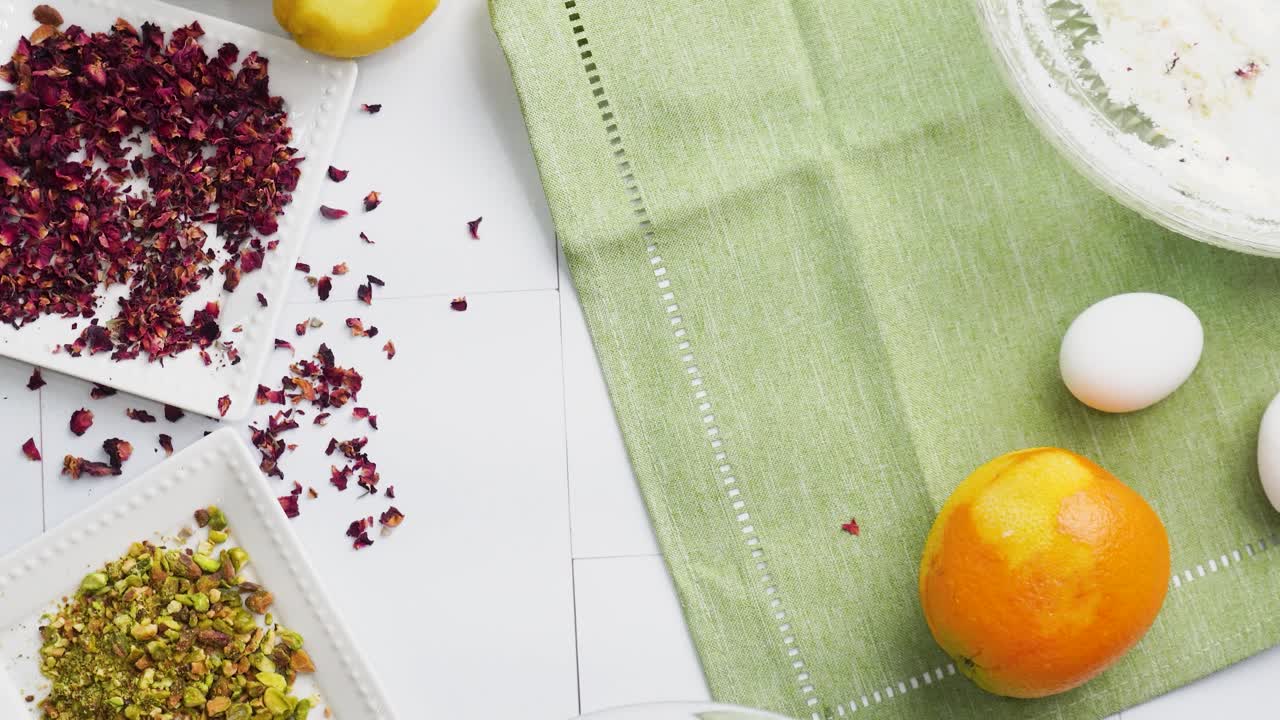 Baking a dessert called Persian Love Cake made with rose petals and pistachios. Cake with white glaze frosting. Placing an empty mixing bowl on the table. Beautiful cake for tea time or celebration