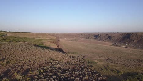 Blue-sky-aerial-over-north-rim-canyon-wall-at-Potholes-Coulee,-WA