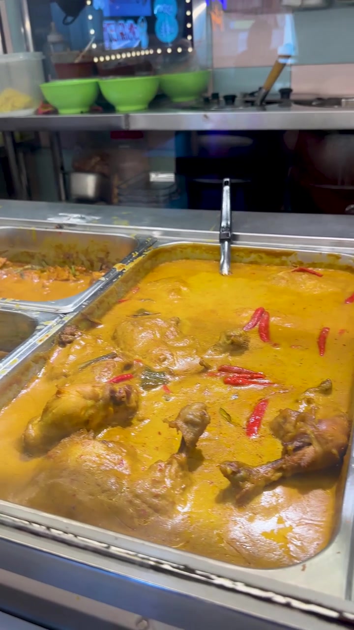 La telecamera panoramica su vivaci vassoi di curry in un ambiente di street food di Singapore illuminato a giorno.