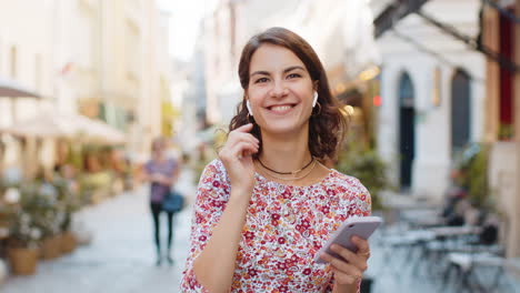 Happy-woman-wearing-wireless-earphones-dancing,-listening-music-in-smartphone-dancing-in-city-street