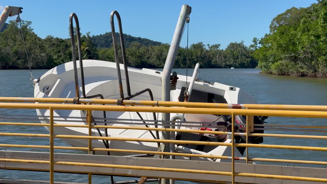 Ferry boat crosses river in bright daylight, worker passes, lush rainforest and calm water background