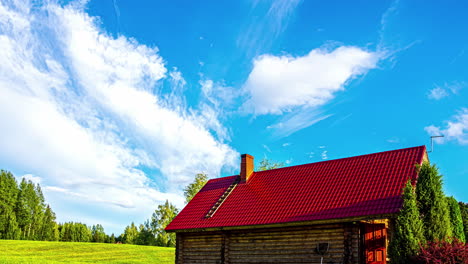 Zeitraffer-Eines-Blauen-Himmels-Mit-Vereinzelten-Wolken,-Der-über-Ein-Bauernhaus-Mit-Rotem-Dach-Und-Grüne-Felder-Zieht