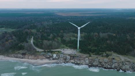 estableciendo una vista aérea de los edificios fortificados abandonados a la orilla del mar en los fuertes del norte de karosta en la playa del mar báltico en liepaja, día nublado, turbina eólica, disparo de dron moviéndose hacia adelante, inclinándose hacia abajo