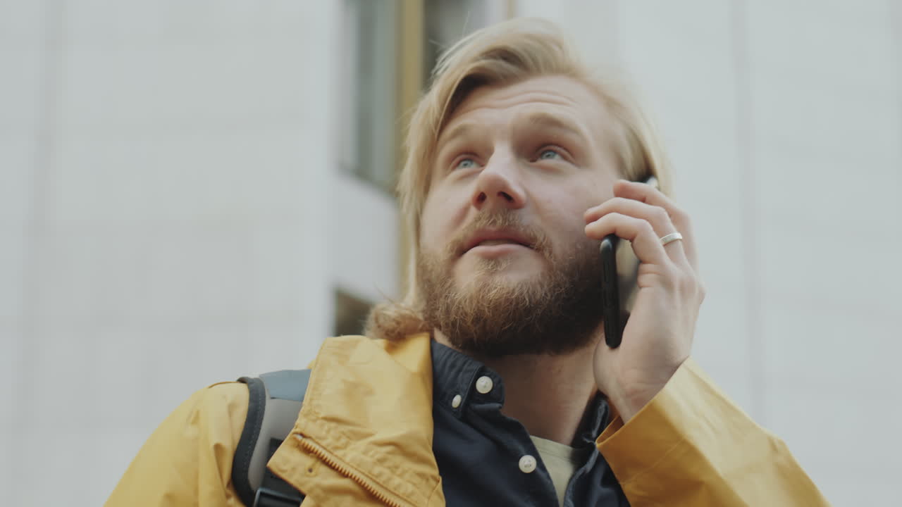 A man with a beard and blonde hair talks on a mobile phone outdoors
