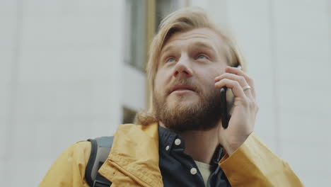 a man with a beard and blonde hair talks on a mobile phone outdoors