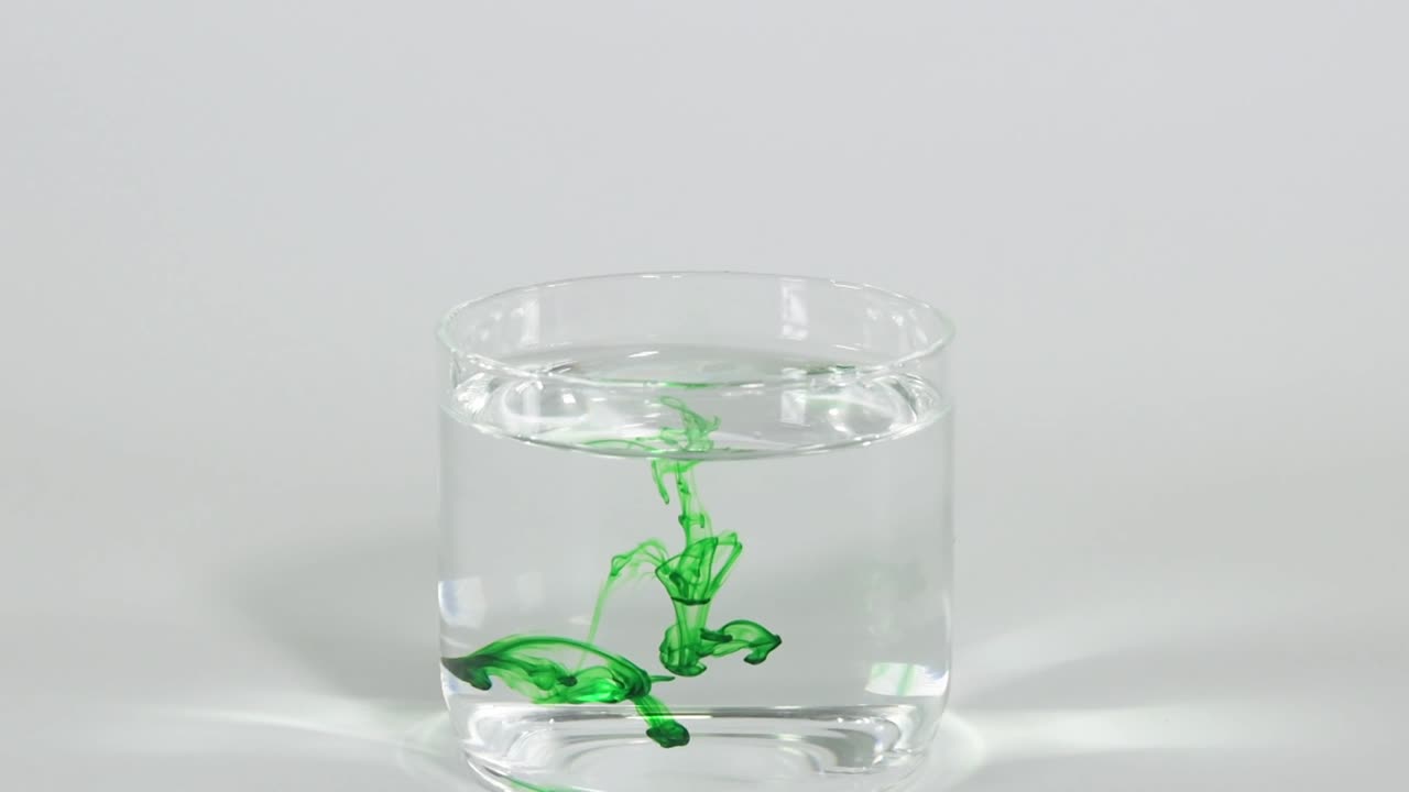 A green toy frog gradually sinks in a transparent glass filled with water, showcasing its descent.