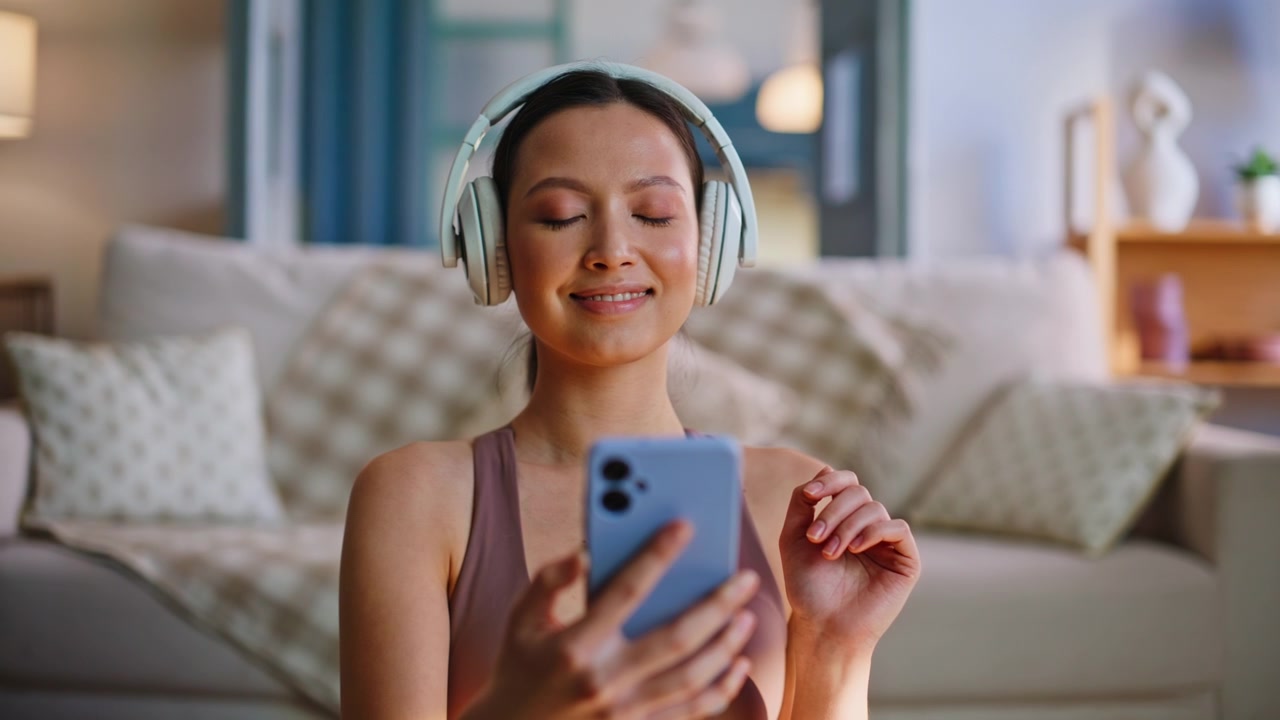 Donna che prende il telefono dopo una sessione di yoga. Ascolta musica in cuffia, relax a casa.