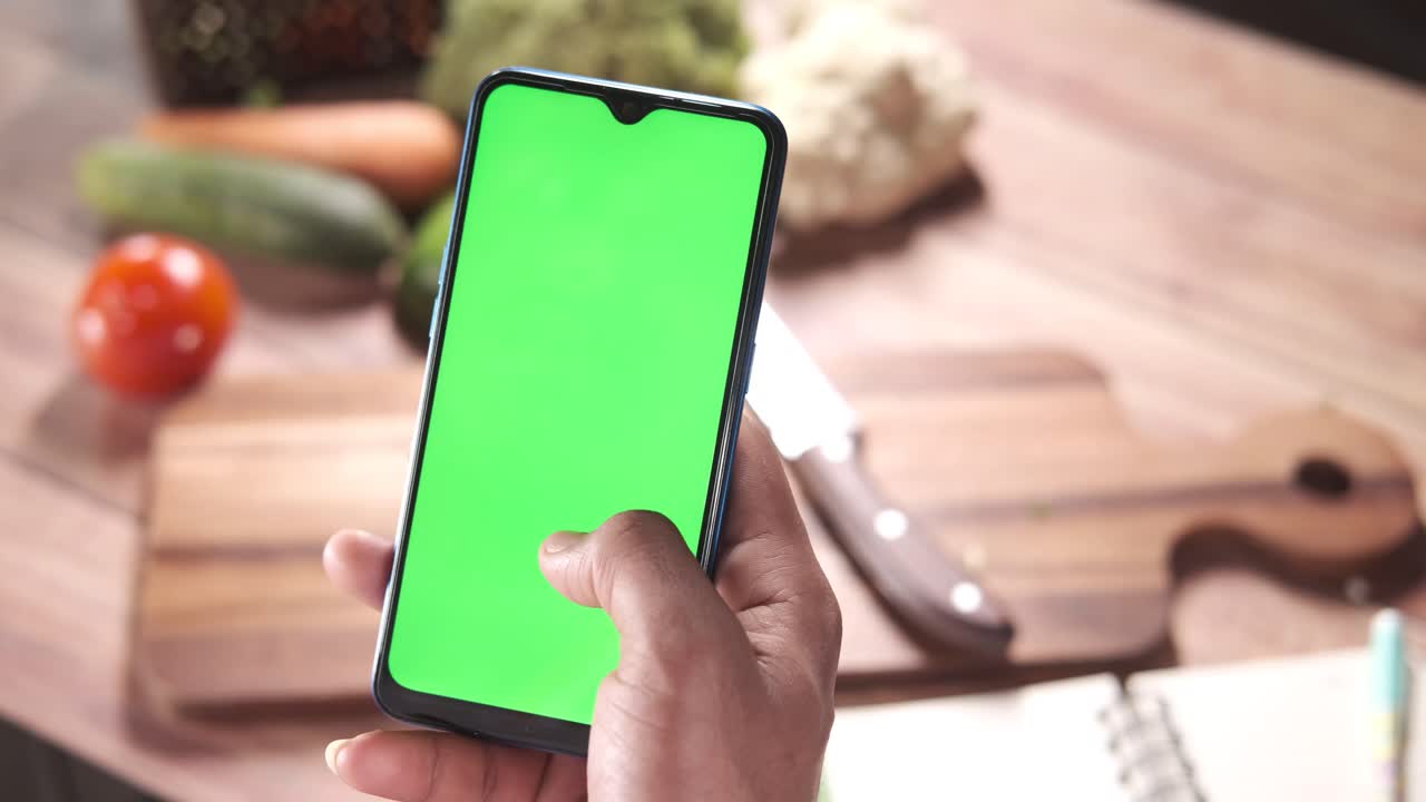 persona usando un teléfono en una cocina con verduras y una tabla de cortar
