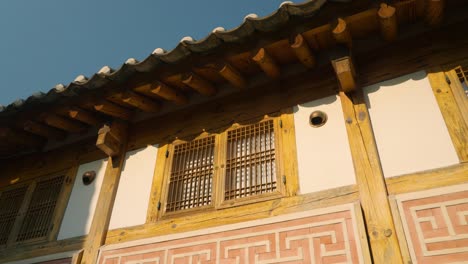 sunlight glints off wooden lattice windows and tiled eaves of a hanok in bukchon hanok village, jongno-gu, seoul