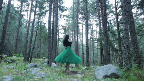 free spirit female wearing green skirt walking in forest and spinning around with arms up in air