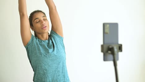 Ethnic-sportswoman-exercising-on-Pilates-ball-against-smartphone