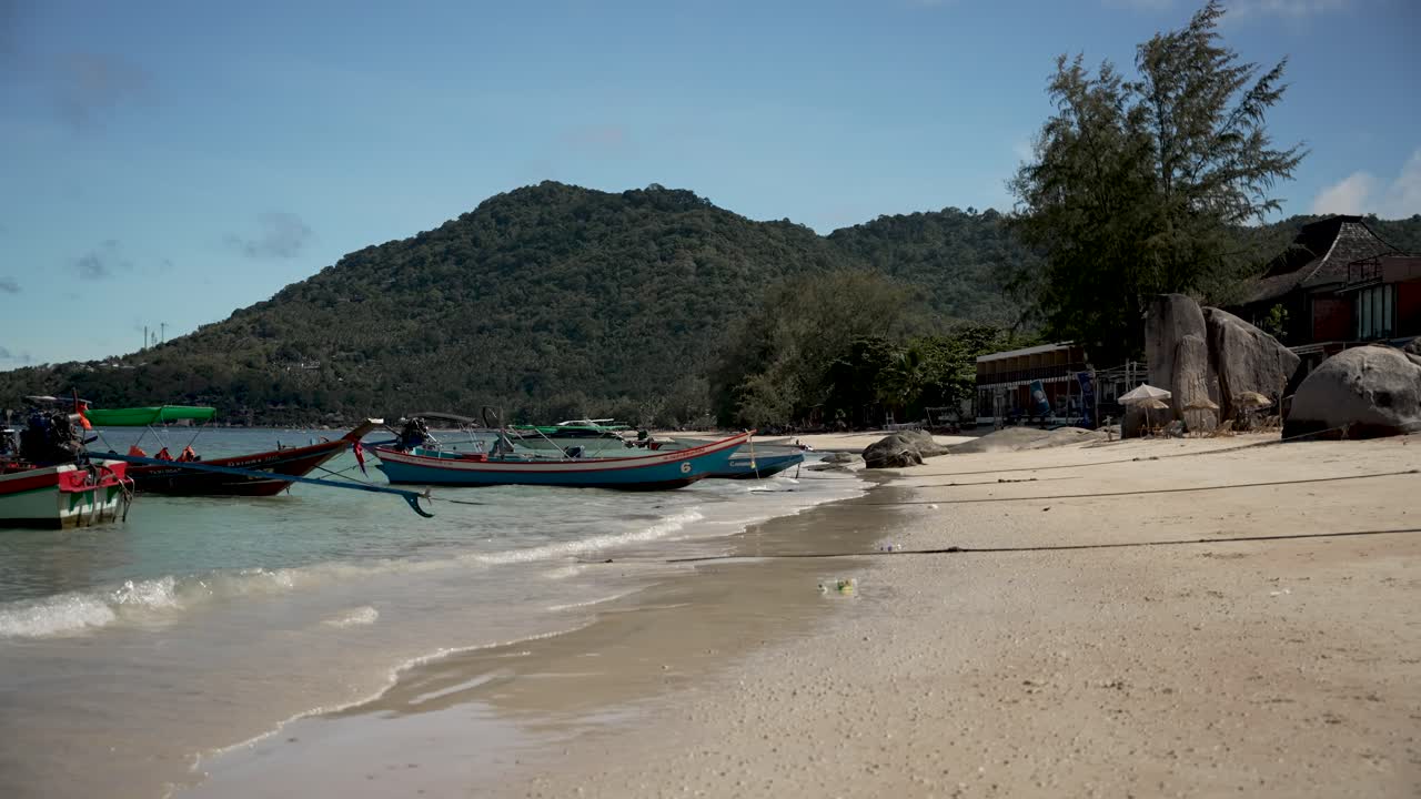 코타오 (koh tao) 의 사리 해변의 아침 풍경. 해안에 정박한 롱테일 보트와 부드러운 파도, 잔잔한 언덕이 배경이다.