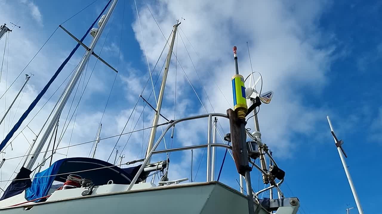 뒤쪽 갑판 레일링에 장착된 회전하는 풍력 터빈 발전기와 함께 요트 마스트를 바라보고 있습니다.