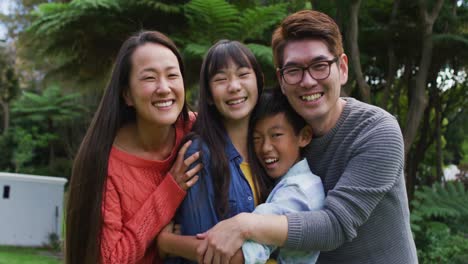 Portrait-of-smiling-asian-parents-embracing-laughing-son-and-daughter-in-garden