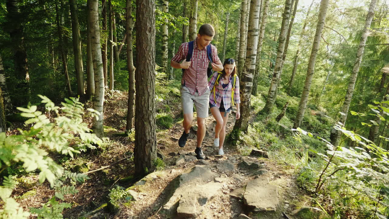 una pareja joven viaja a lo largo de un lugar pintoresco en el bosque un hombre ayuda a una mujer a caminar por el