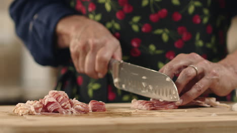 Bacon-being-chopped-with-a-knife-on-a-cutting-board-by-woman-in-apron