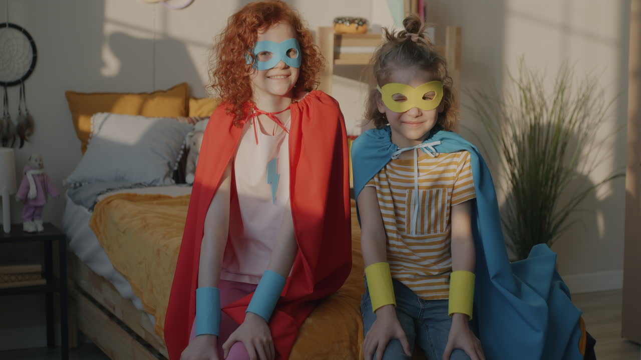 Two girls dressed as superheroes sitting on a bed