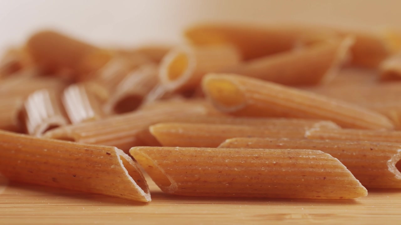 Pasta integrale biologica, maccheroni di semola di grano duro, penne rigate crude in una ciotola di legno. Filmato 4k di alta qualità