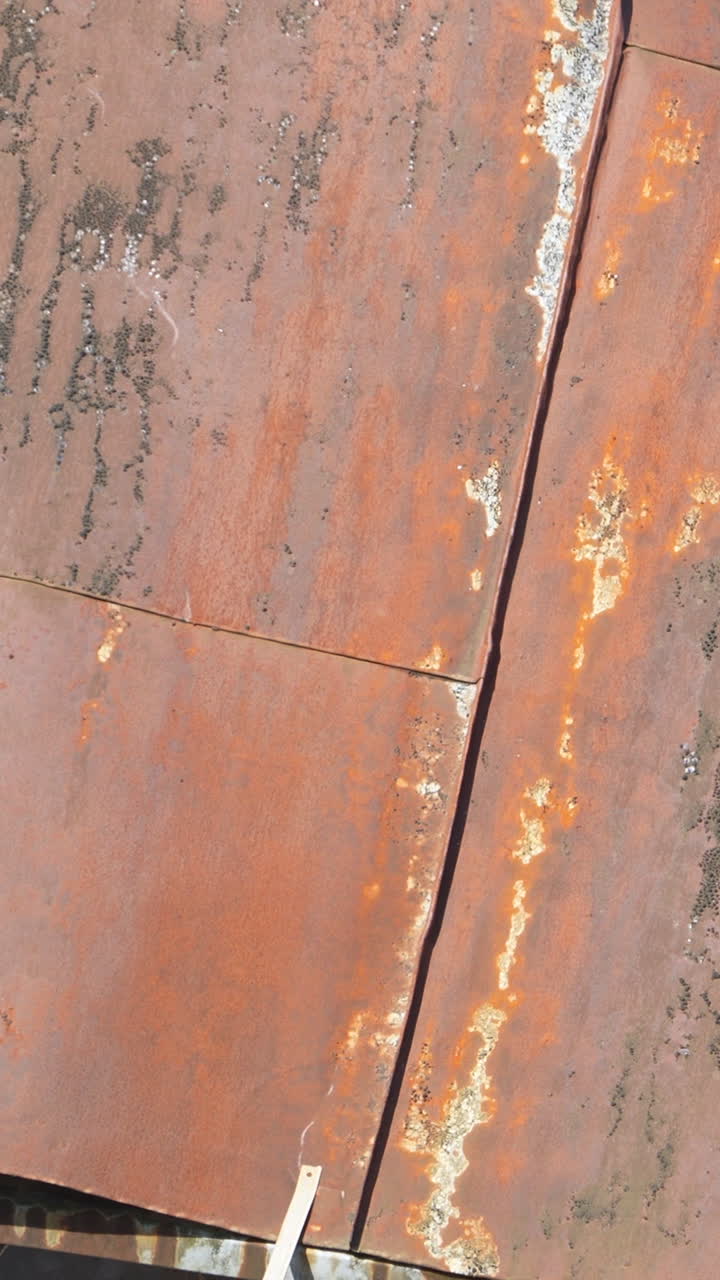 En kraftig hydraulisk gravemaskine med gribeklo river en forvitret rusten metalbygning ned. Filmisk nærbillede af industriel nedrivning og rydning af byggeplads.