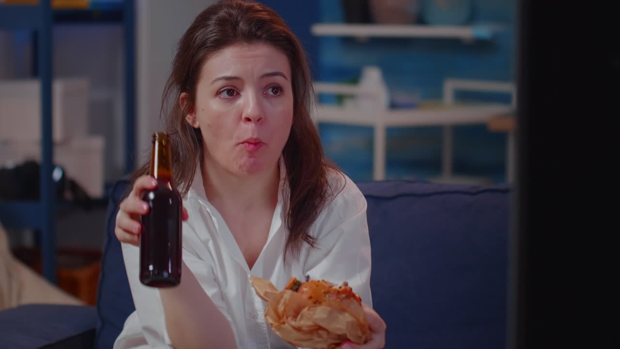 Portrait of young woman eating burger and drinking beer
