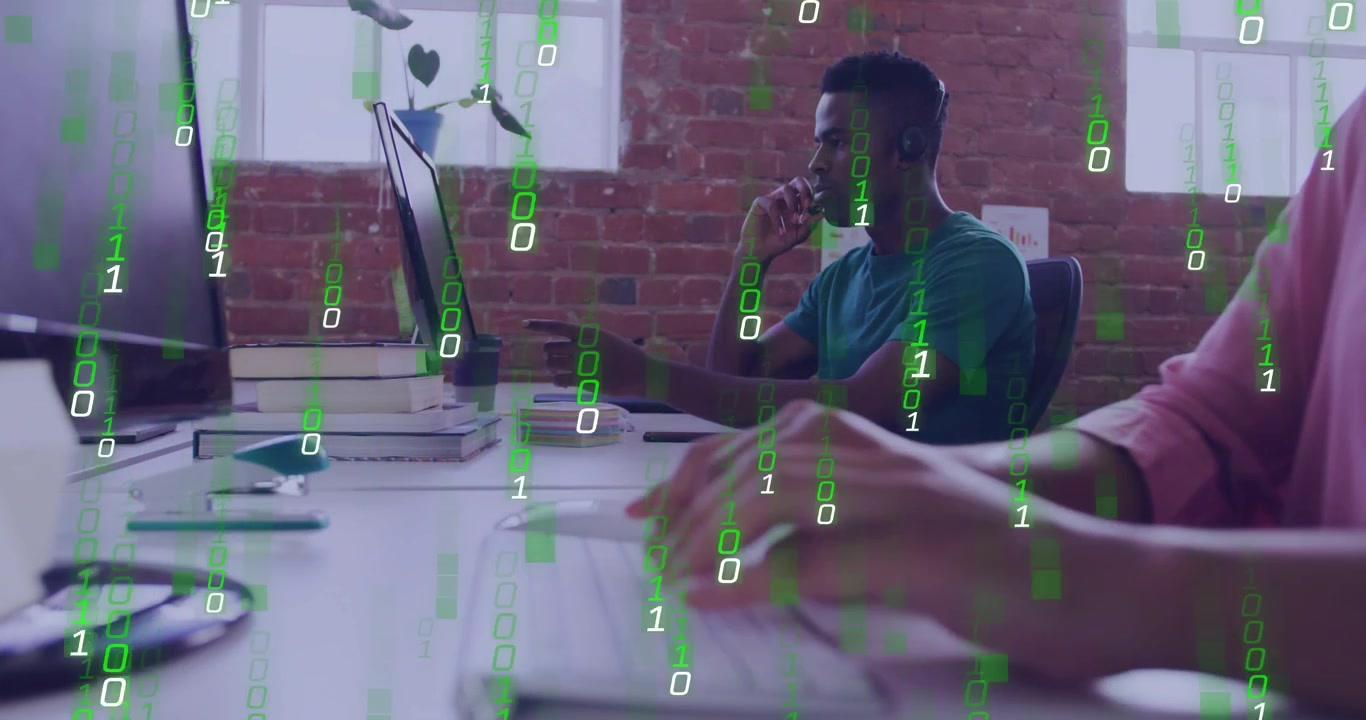 Un homme parle au micro, pointe un moniteur technologique, ce qui provoque une superposition de code binaire tandis qu'un collègue tape du code.