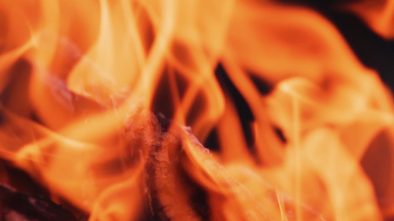 Close-up blur bright flame. Vivid flame of bonfire on dark background. Detailed motion of yellow and red fire. Slow motion.