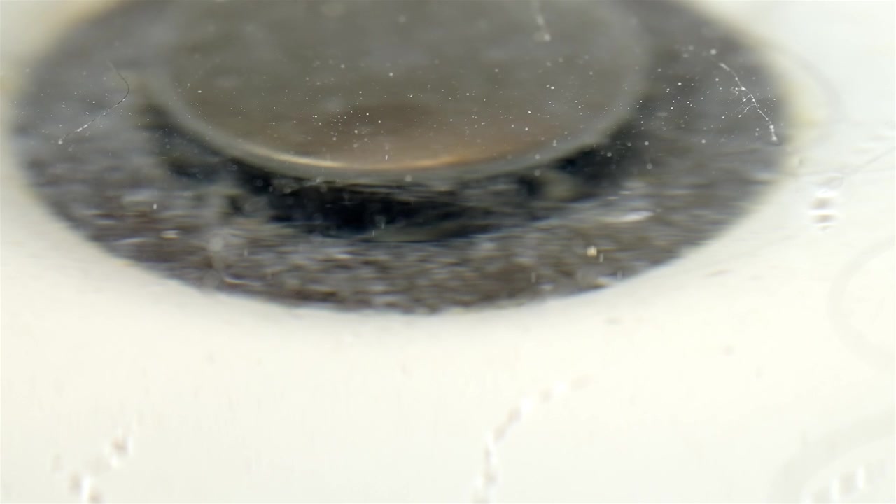 Blurry close up of a dirty bathtub drain with hair and flowing water