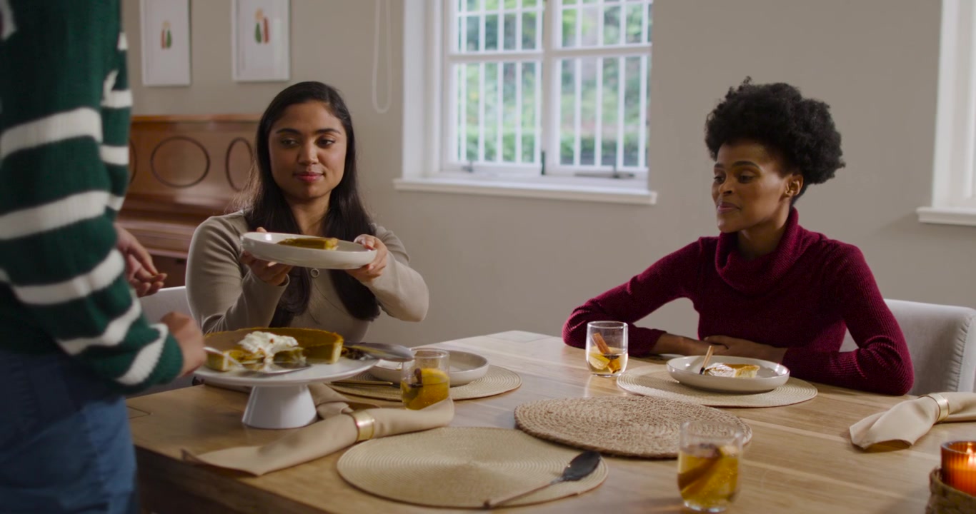 Diverse female friends receiving cake, server with cake stand serving with spatula at dinner table