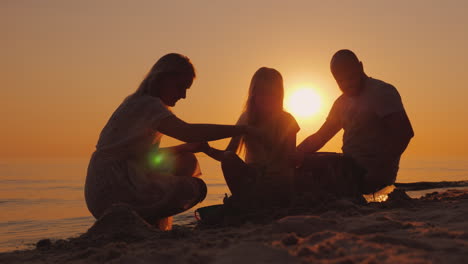 parents play with daughter in the sand near the sea build together a sand castle