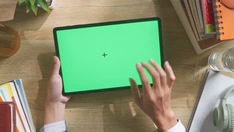 vista de arriba hacia abajo de una computadora portátil con pantalla verde simulada pantalla chromakey en un escritorio de oficina de madera al lado de la libreta con bolígrafos, gafas y un vaso de agua.