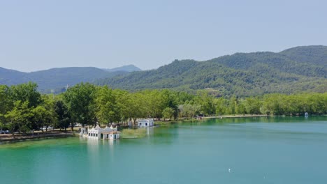 Amplia-Vista-Aérea-Sobre-El-Lago-Banyoles-Casas-De-Botes-Y-Las-Montañas-En-El-Horizonte