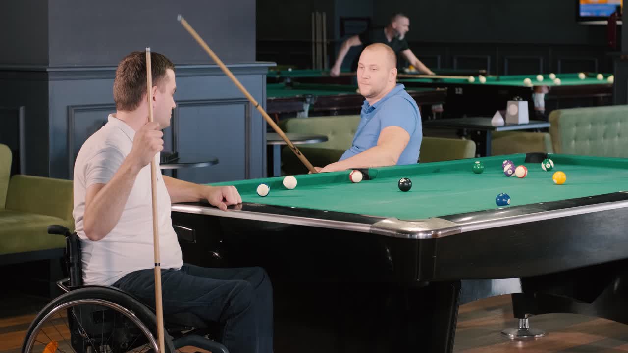 체어에 앉아 있는 장애인 성인 남성들이 클럽에서 빌리어드를 치고 있습니다.