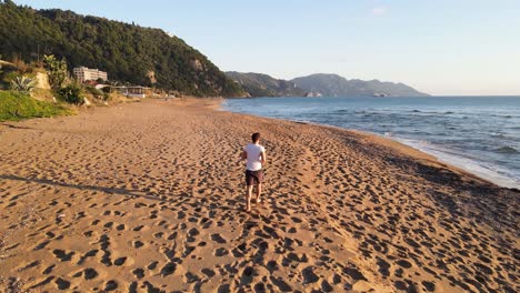 Man-running-on-an-empty-beach,-filmed-from-behind-at-afternoon-summer-time