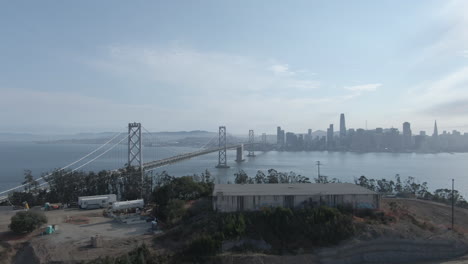 Schwenk-über-Die-Skyline-Von-San-Francisco-Und-Die-Bay-Bridge-Aus-Der-Sicht-Eines-Mavic-Pro-Drohnenflugs-über-Yerba-Buena-Und-Treasure-Island-An-Einem-Dunstigen-Sommernachmittag---4k---Flache-Farbe