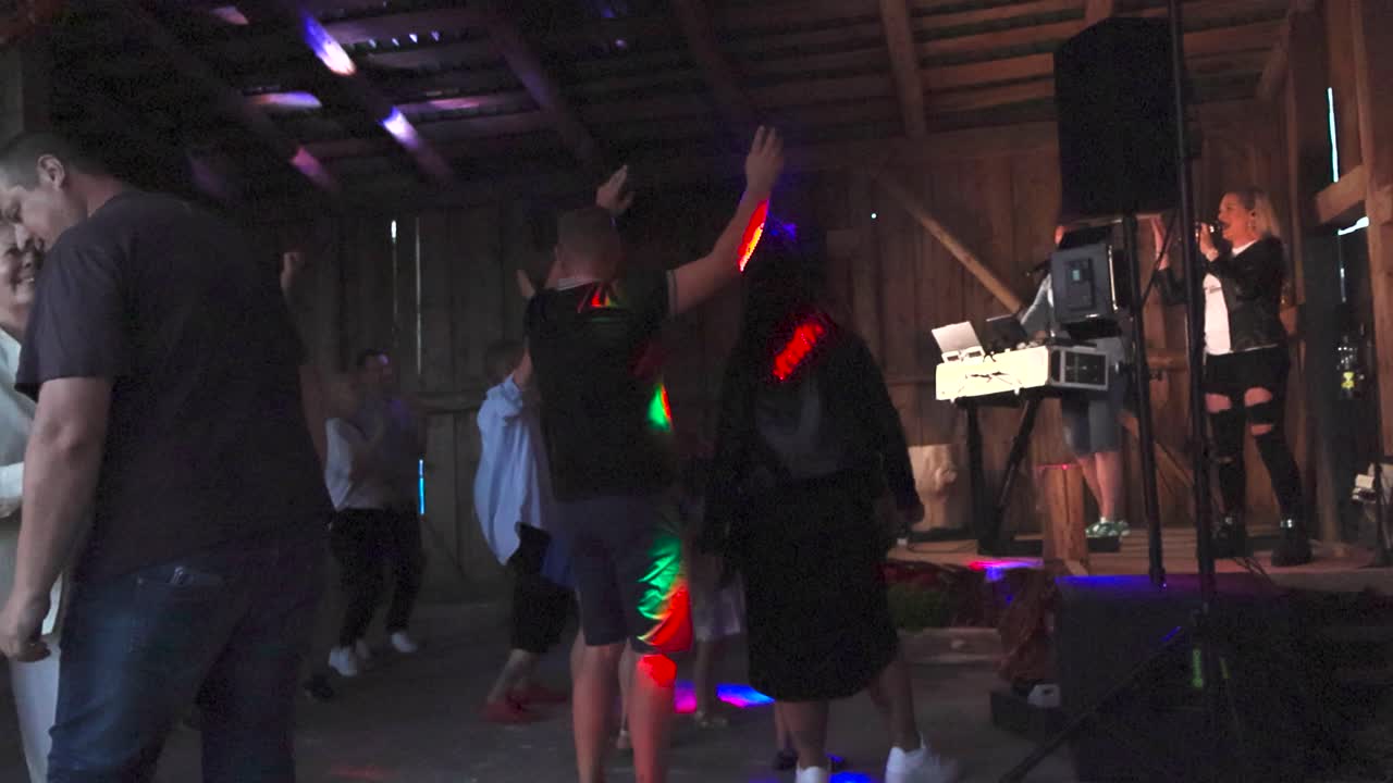 People jumping and listening to a local band called Kurjad Plaanid in a wooden barn during a concert. Strobe lights and spot lights are lighting the room and footage is in slow motion during summer.