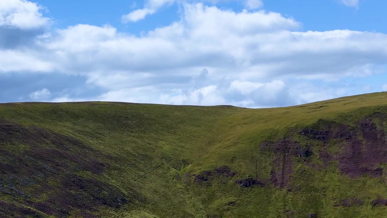 Una vista cinematografica di dolci colline verdi e terreno accidentato sotto luminose nuvole estive.