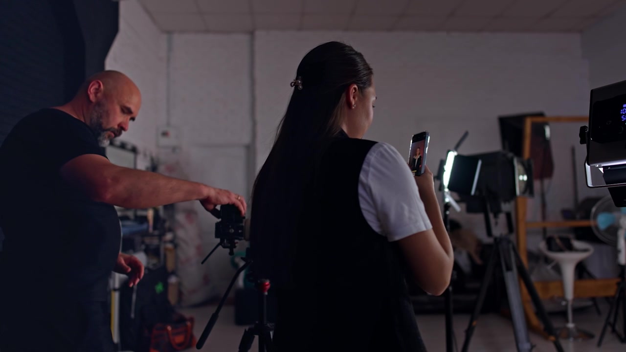 Woman taking video on her phone and man uses a professional camera. Blog video creation in studio.