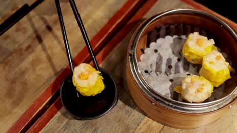 chopsticks picking dumplings from a bamboo steamer