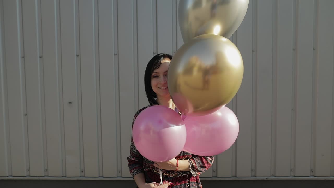 mujer bonita en vestido sosteniendo globos con helio al aire libre a la luz del día