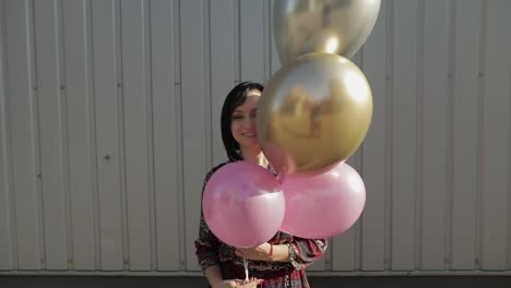 mujer bonita en vestido sosteniendo globos con helio al aire libre a la luz del día